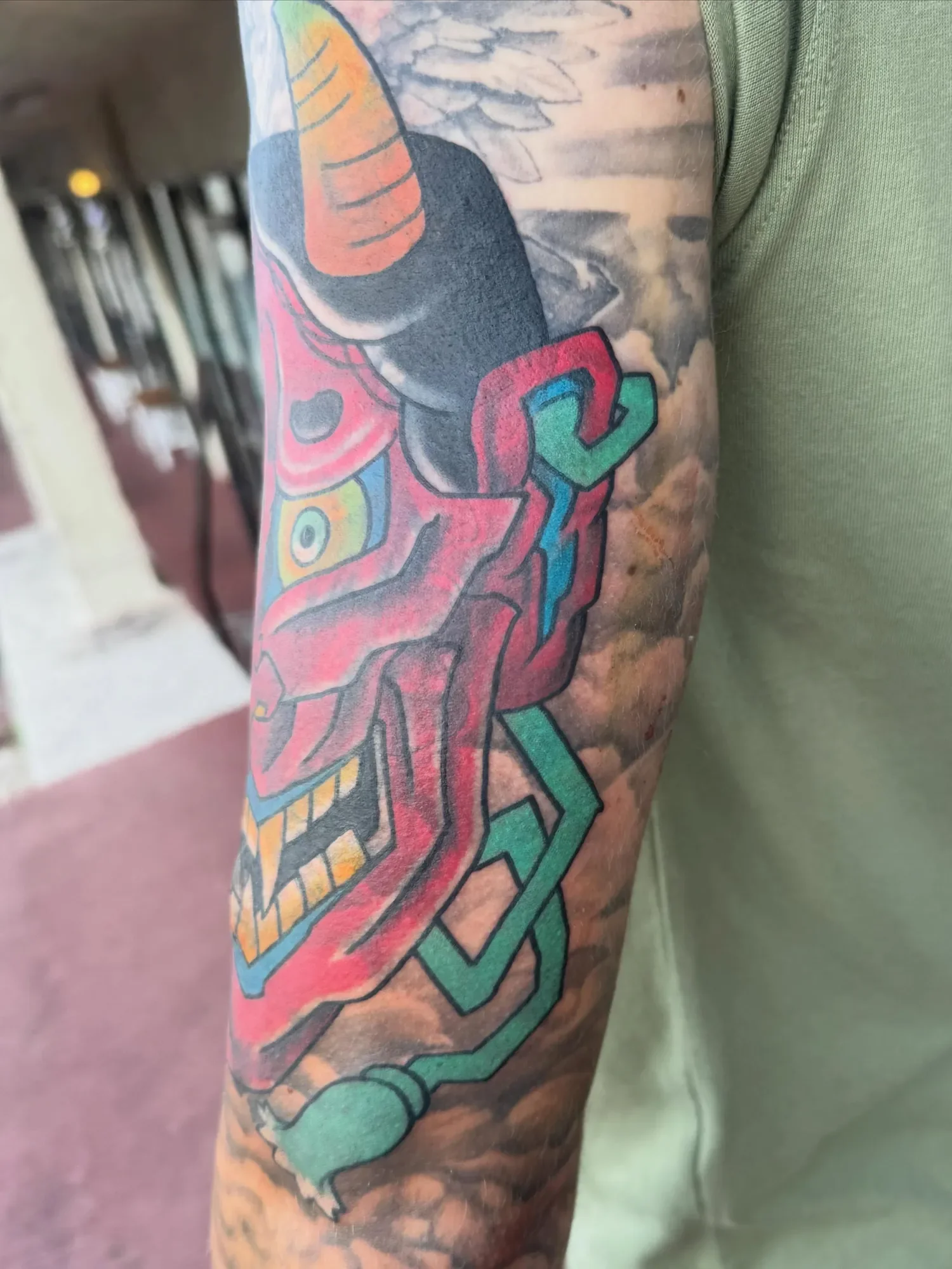 Close-up of a colorful tattoo on a person's arm, featuring abstract, geometric, and illustrative elements with various colors including red, green, black, and orange.