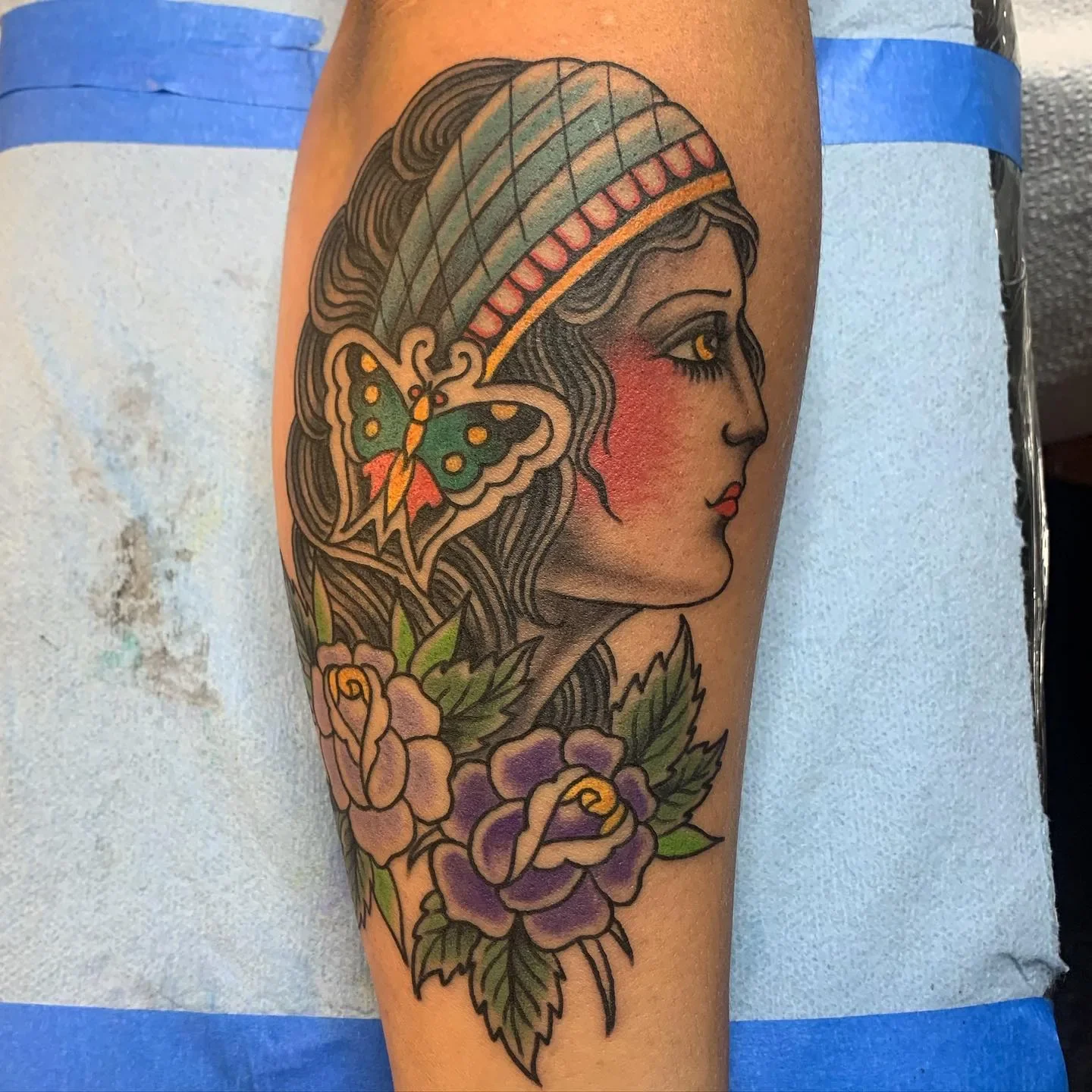 Traditional gypsy style lady head profile with butterfly hair ornament and purple roses. Classic color traditional portrait tattoo by Brett Semrick.