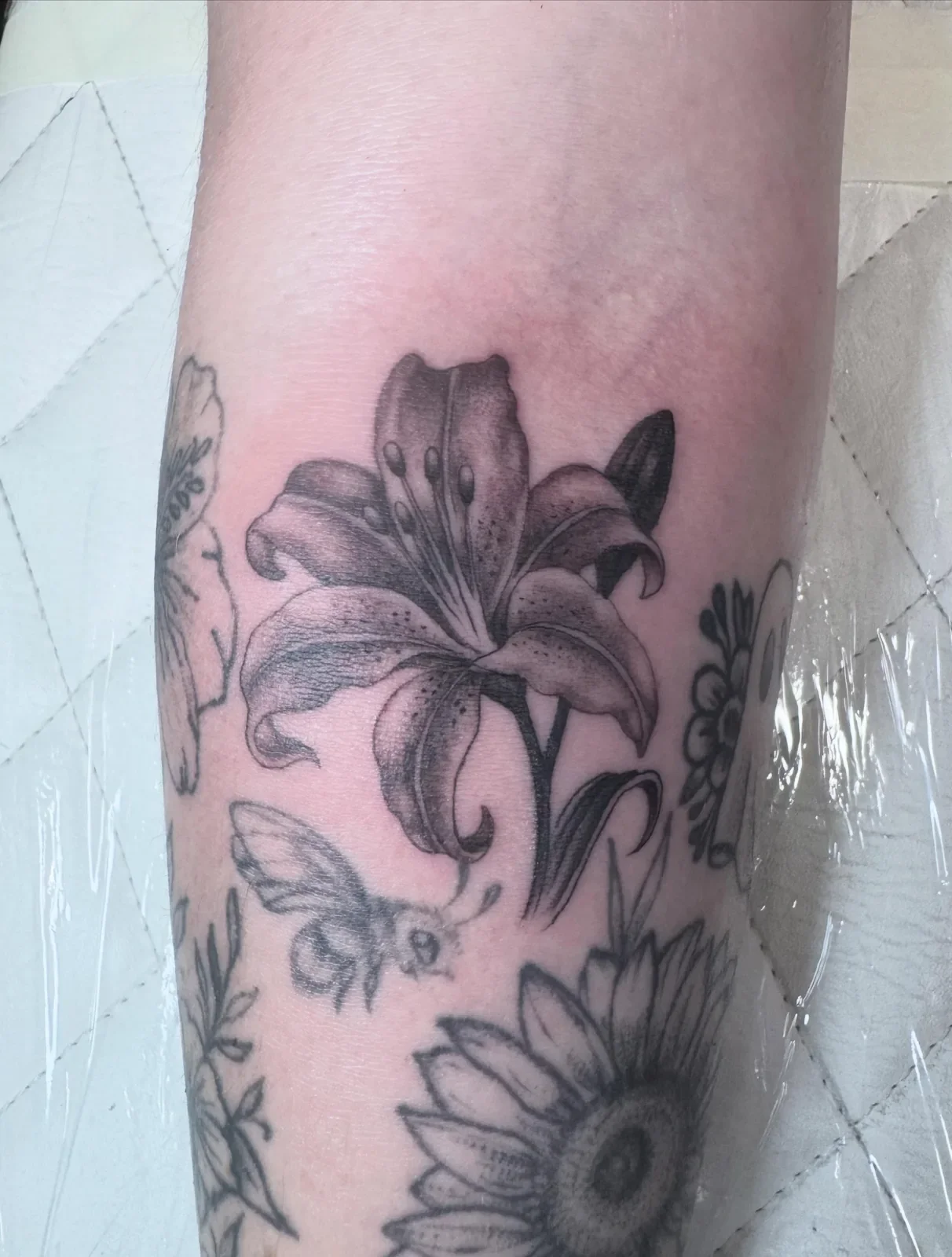 Soft black and gray realistic lily flower tattoo with fine dotwork shading, perfect gap filler between existing florals. Detailed botanical work by Brett Semrick.