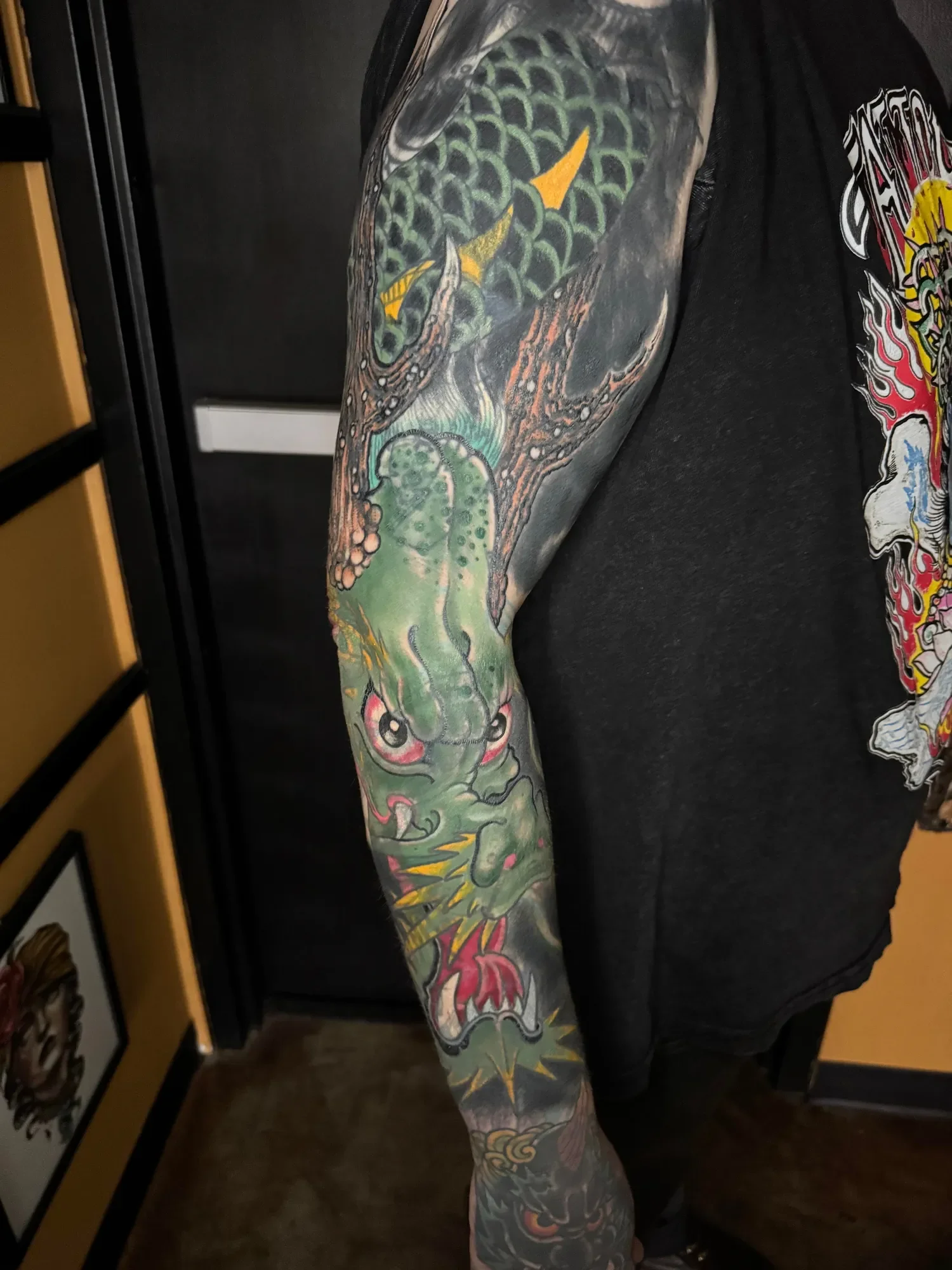  Full sleeve dragon — green scales with yellow horns, black and grey smoke fill, winding from shoulder to wrist. Healed and settled, bold traditional Japanese.