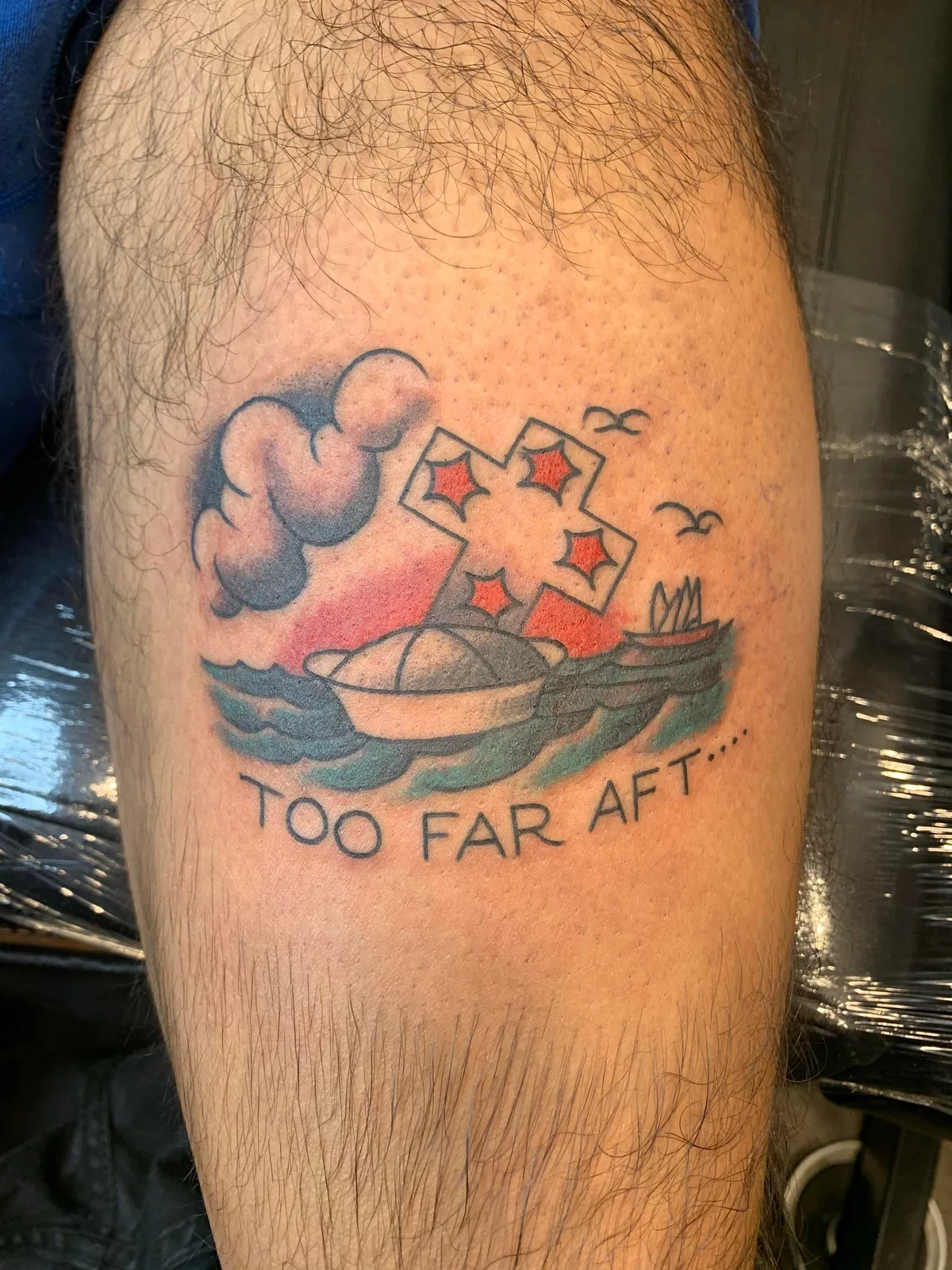 Humorous trad — diamond-pattern cross sinking a sailor cap with "TOO FAR AFT..." below. Sunset wash and seabirds.
