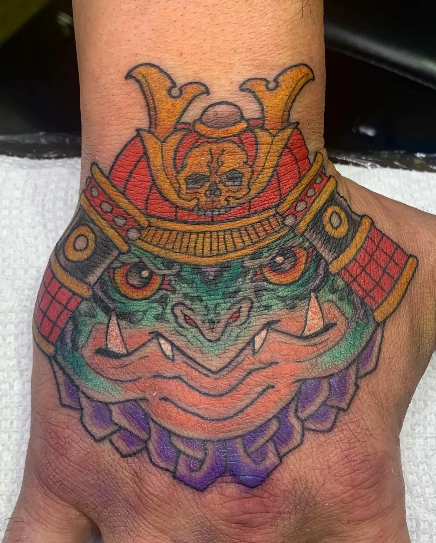Samurai frog hand piece with red kabuto, skull crest, and purple bead collar. Heavy saturation for a small canvas.