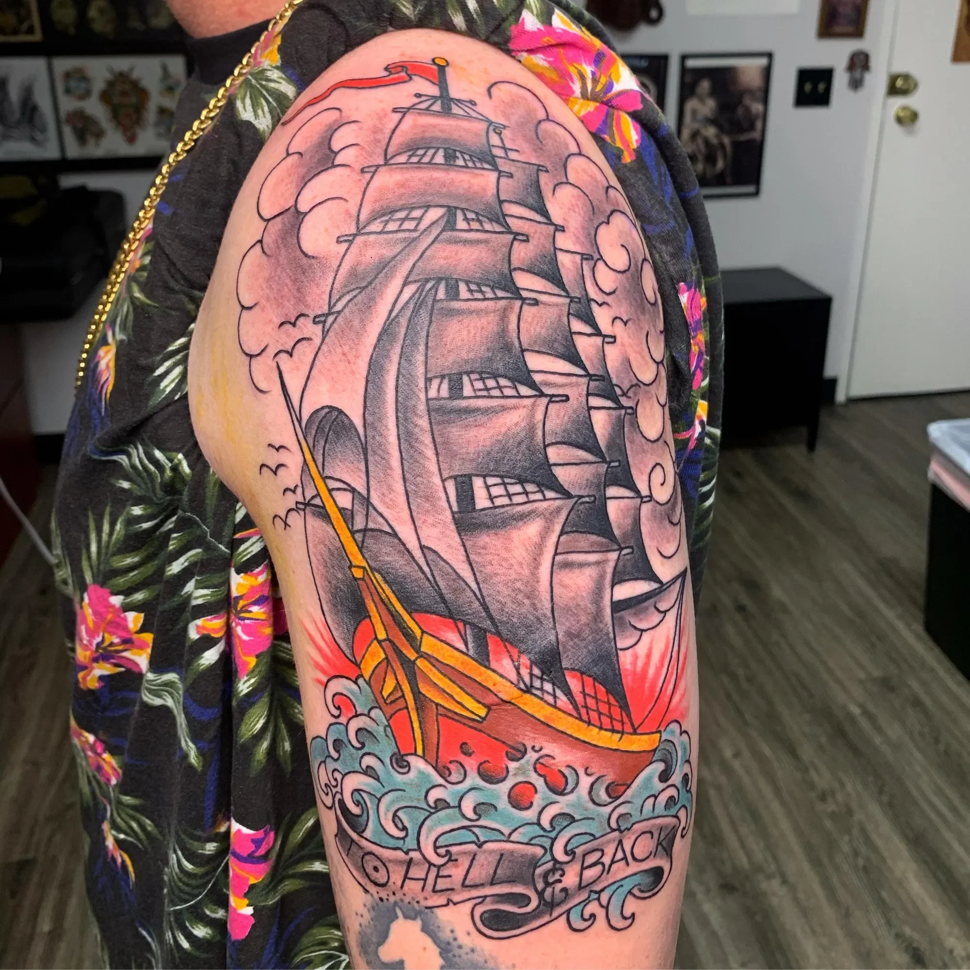 A tattoo of a sailing ship surrounded by colorful clouds on a person's upper arm.
