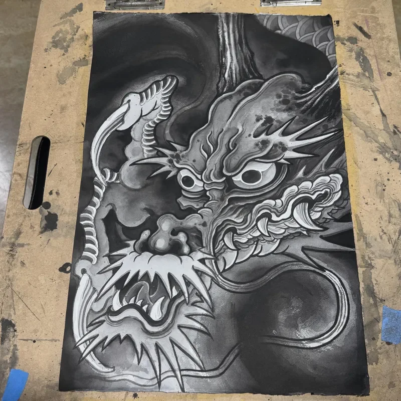 Intense black and grey close up of Japanese ryu dragon head with detailed whiskers, fangs, spiked mane and wild eyes emerging from darkness and seigaiha pattern. Heavy sumi wash with white highlights.

