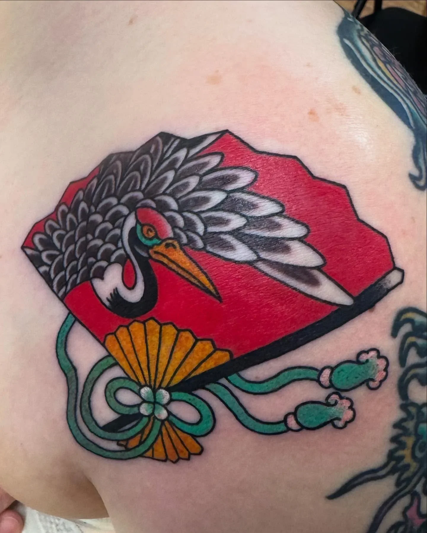 Colorful traditional Japanese style tattoo of a crane bird with a red background with floral and wave patterns.