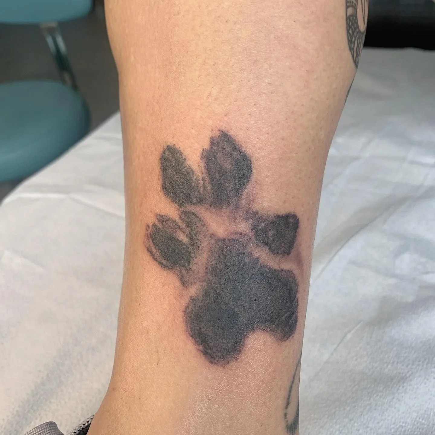 Tattoo of a black paw print on a person's forearm.