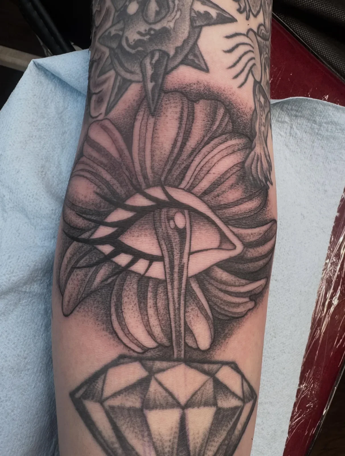 Black and gray tattoo of a stylized moth with a diamond below it on a person's arm.