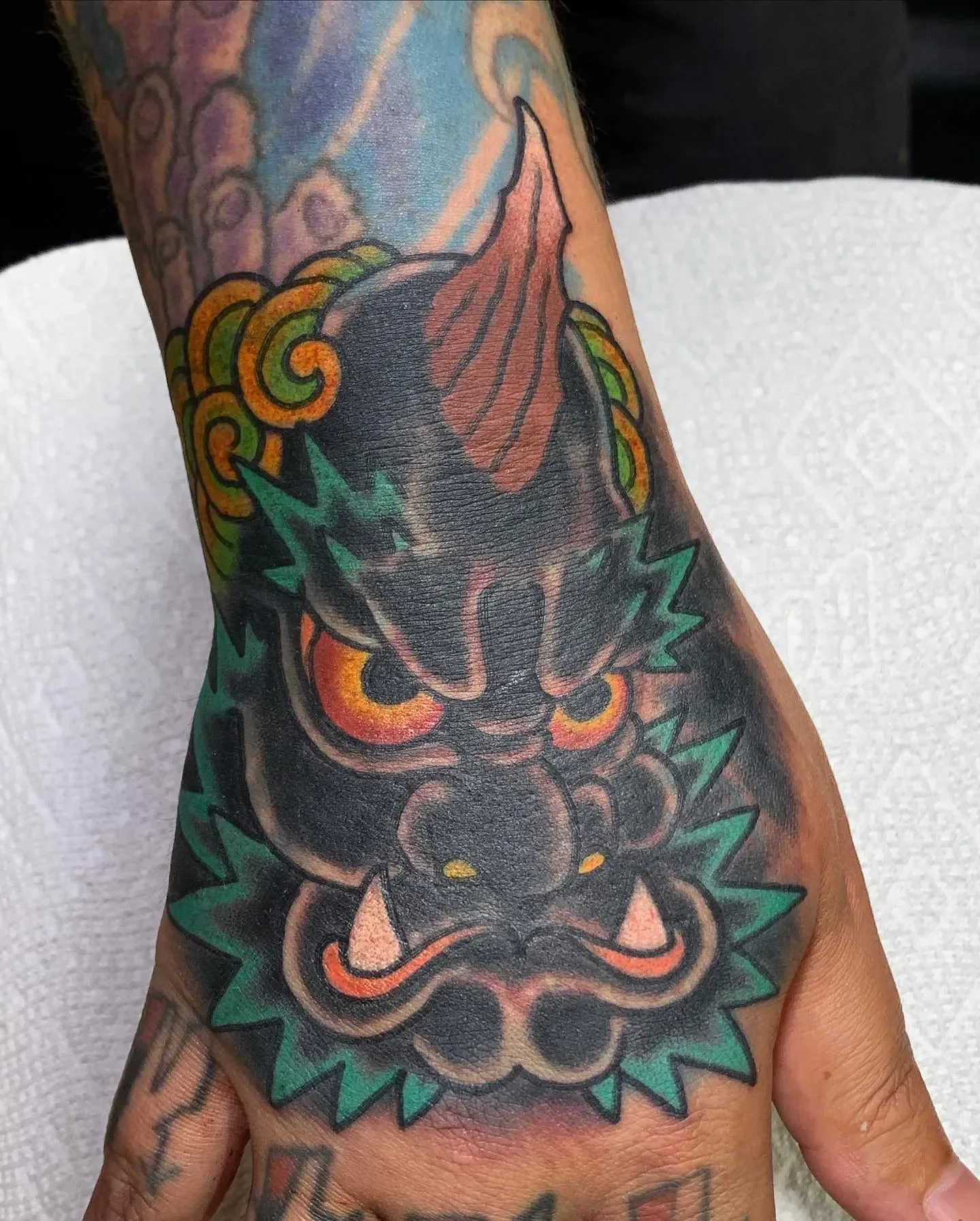 Tattoo of a dragon on a person's arm, with colorful details including green accents and an orange-red crest.