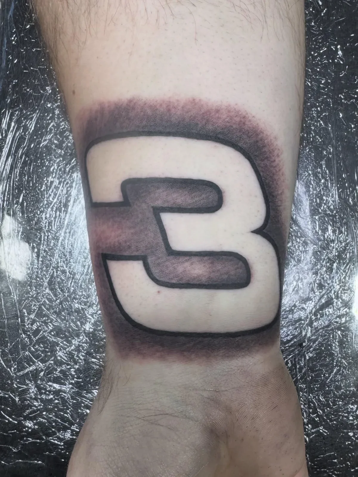 Bold number 3 tattoo in large block font with negative space and soft blackwork shading background. Clean custom number piece by Brett Semrick.
