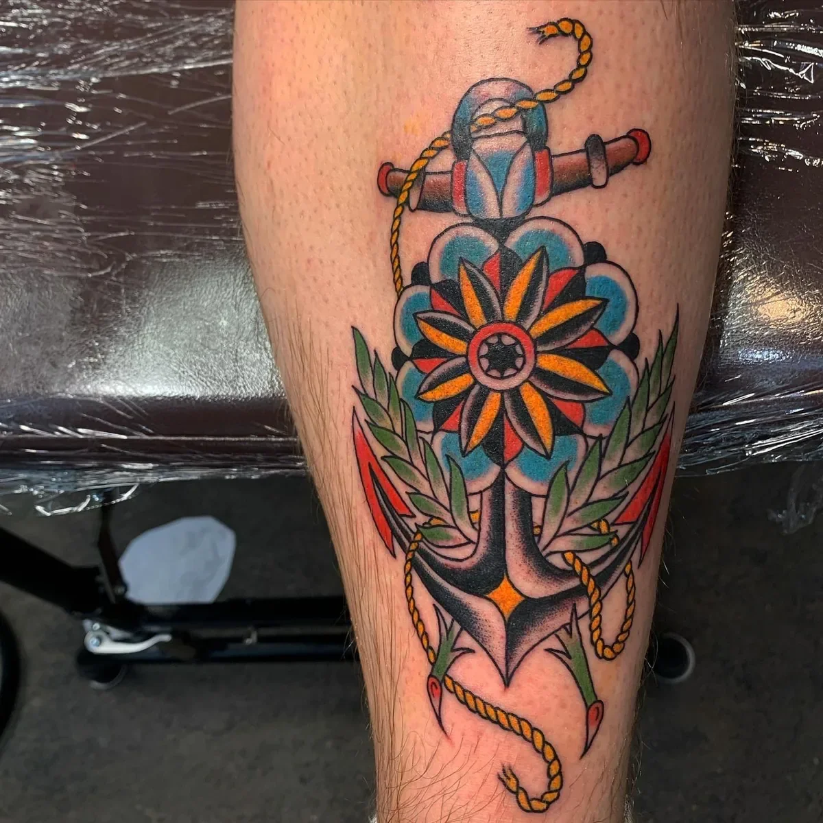 Bold American Traditional anchor tattoo with stylized flower, laurel leaves and yellow rope. Full color traditional work by Brett Semrick in San Diego.