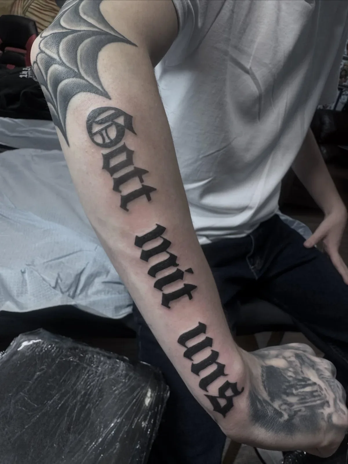 Bold blackwork Old English gothic lettering tattoo reading Gott mit uns down the outer forearm. Solid black traditional lettering piece by Brett Semrick.