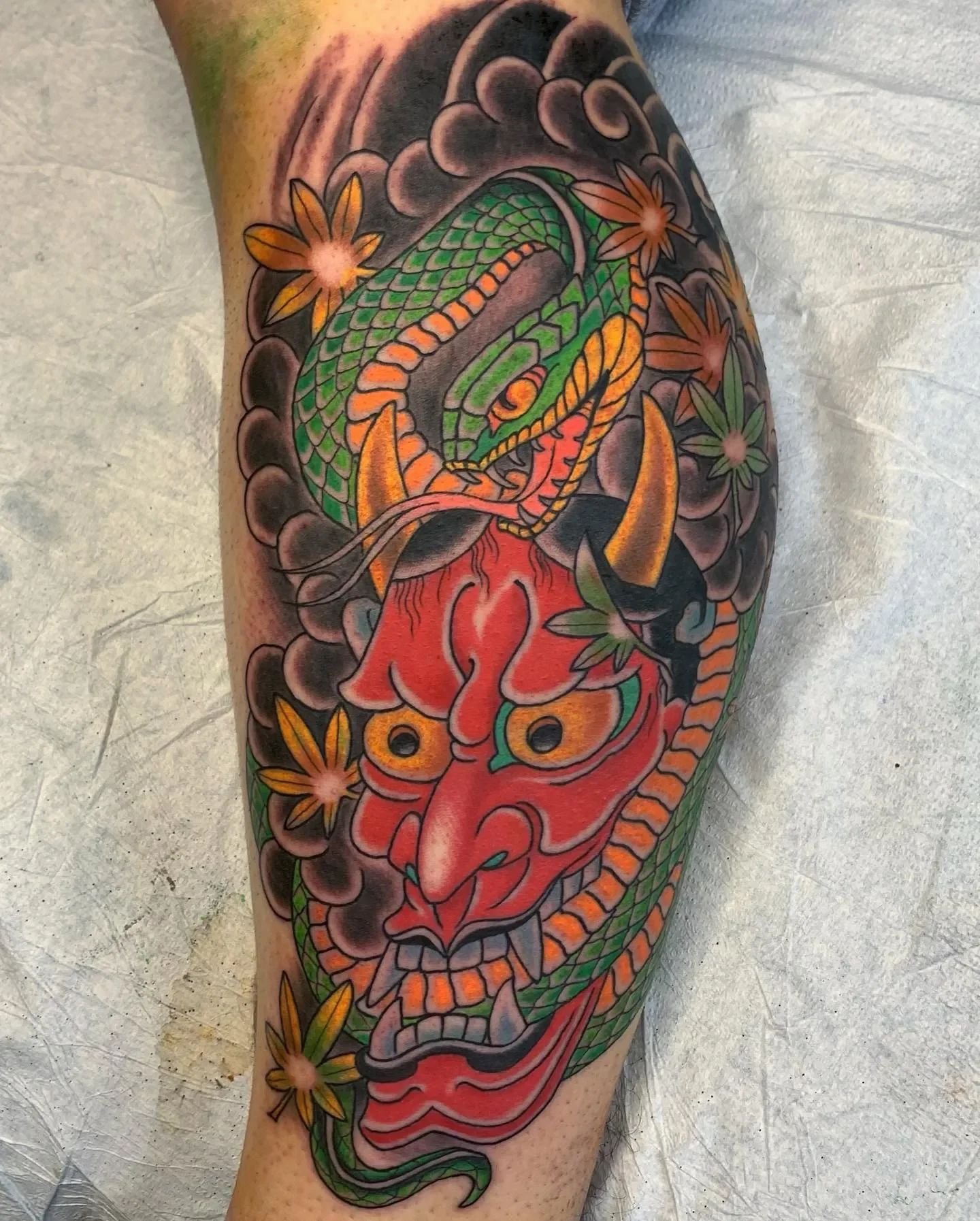 Red Hannya wrapped in green snake with momiji and wind bars. Full color Japanese leg piece with contrast and flow built for the calf.