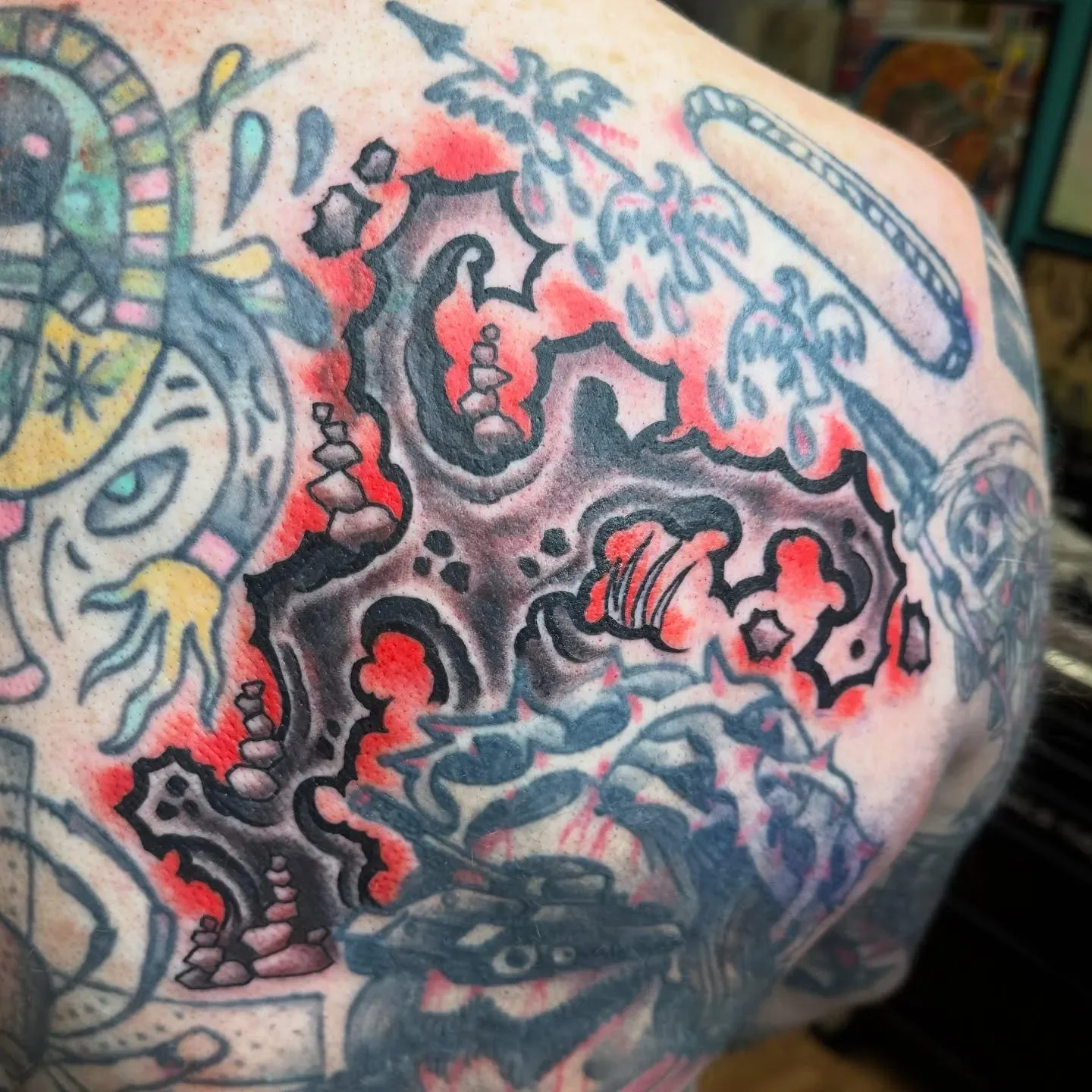 Close-up of a colorful tattoo with various designs, including a snake, skull, palm trees, and other intricate patterns with black, red, and yellow ink.