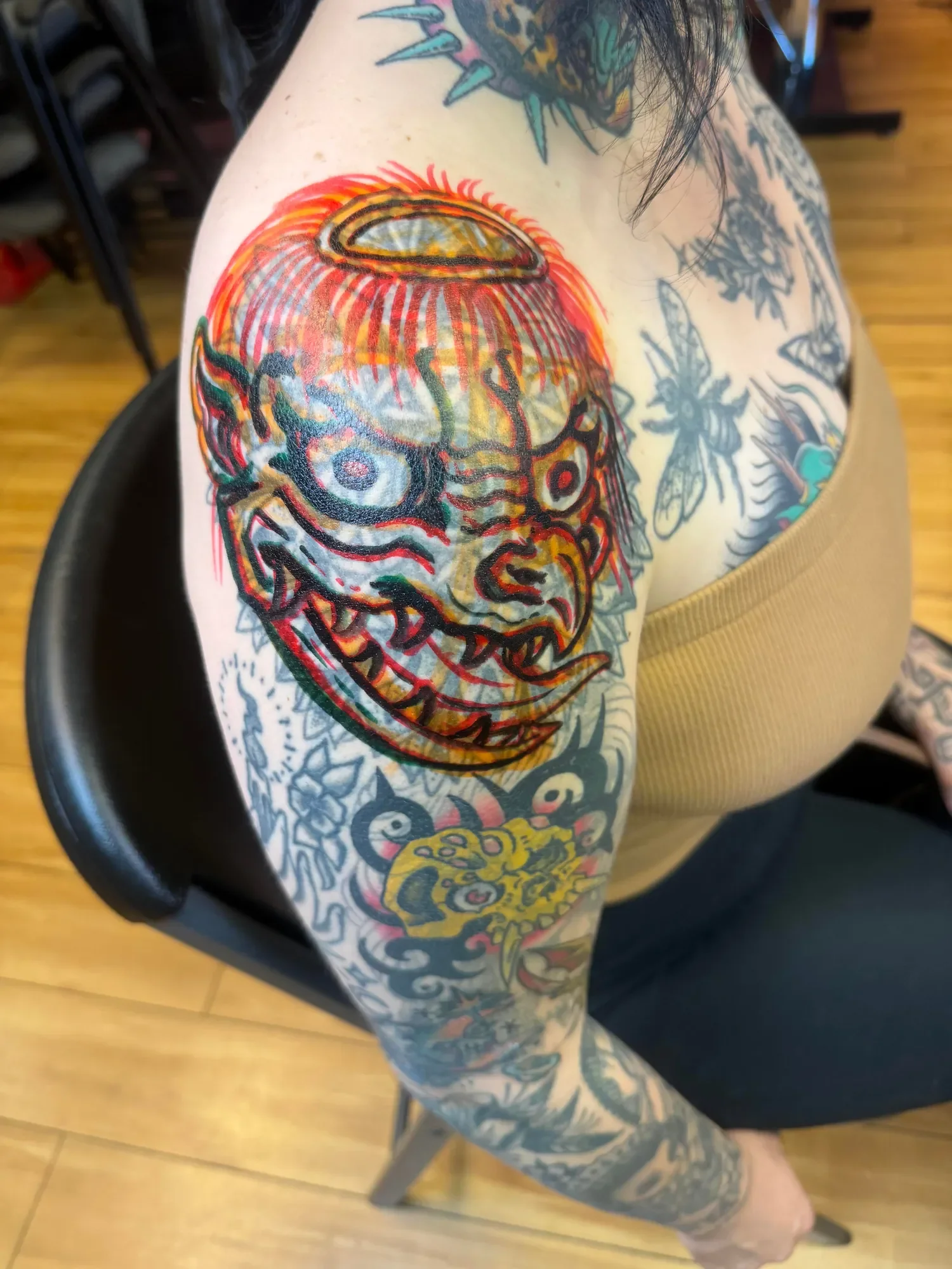 Colorful tattoo sleeve featuring a dragon, a lion, and various other designs on person's arm and shoulder.