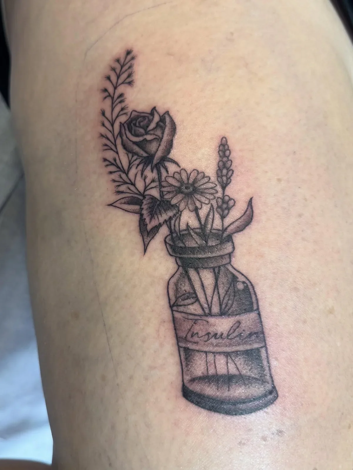Tattoo of a plant arrangement in a jar, featuring a rose, daisy, lavender, and leaves.