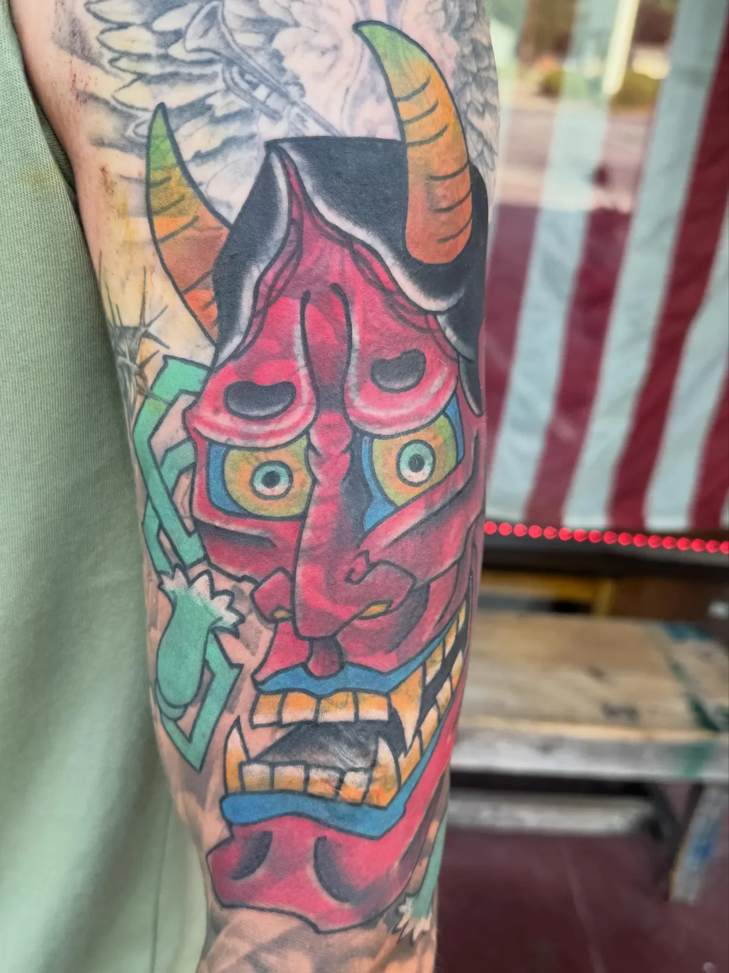Colorful tattoo featuring a geometric horned animal with pink, orange, and green accents on a person's arm.