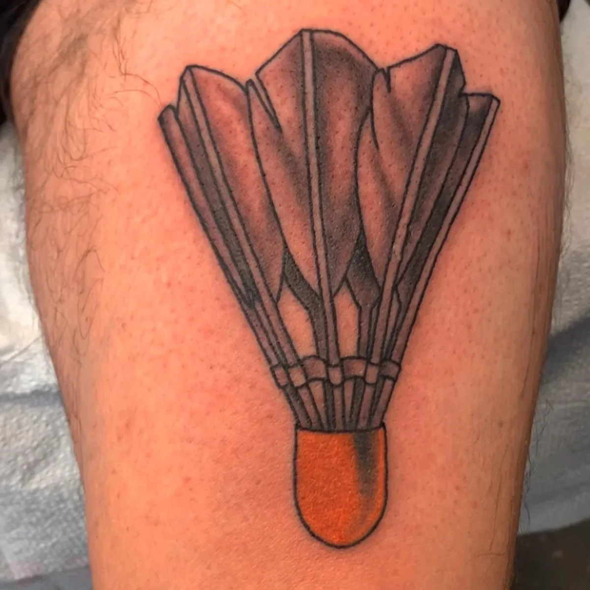 Custom illustrative shuttlecock tattoo in black and grey with orange color pop. By Brett Semrick, San Diego tattoo artist specializing in clean linework and playful small tattoos.