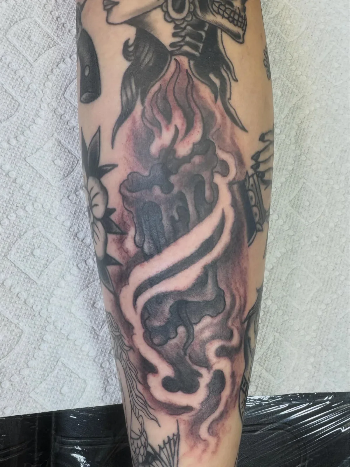 Tattoo of a skull with flames and smoke design on a person's arm.