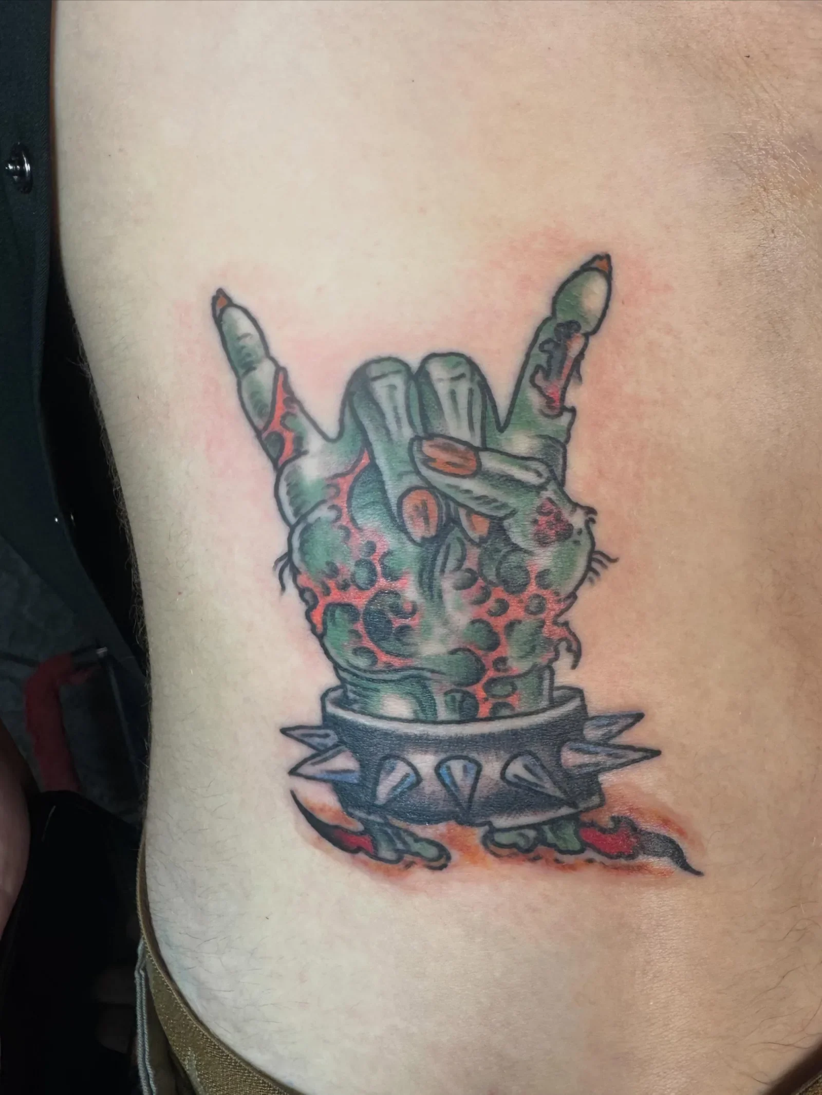 Color traditional zombie hand doing rock horns with spiked cuff and green decay. Bold horror punk tattoo by Brett Semrick 