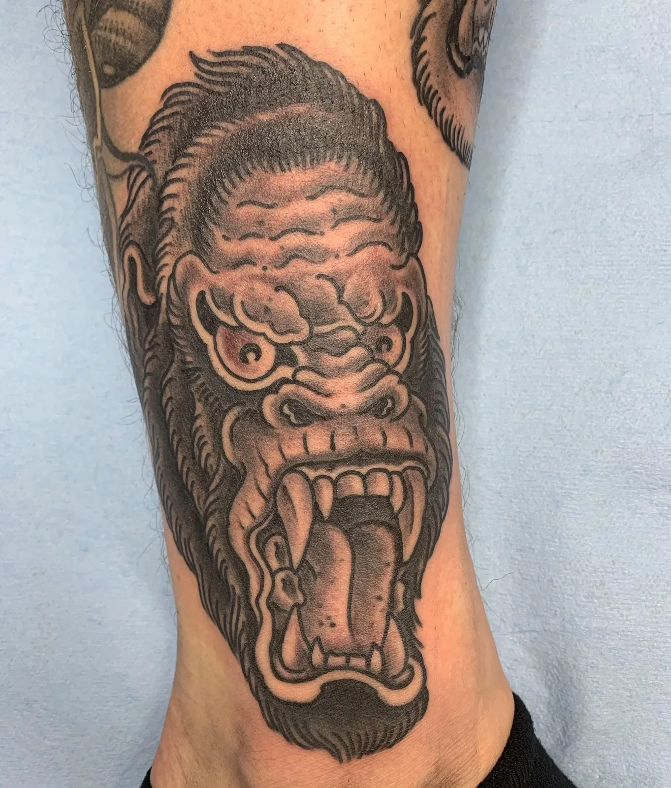 Roaring gorilla in bold blackwork trad style — heavy whip shading and exaggerated expression.
