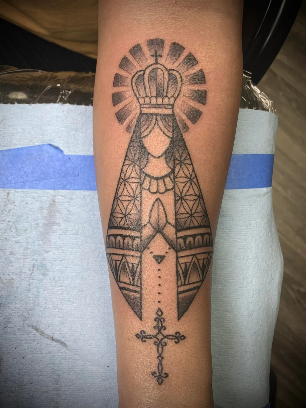 Stylized Virgin in linework trad — crown, halo rays, sacred geometry robe and ornate cross.
