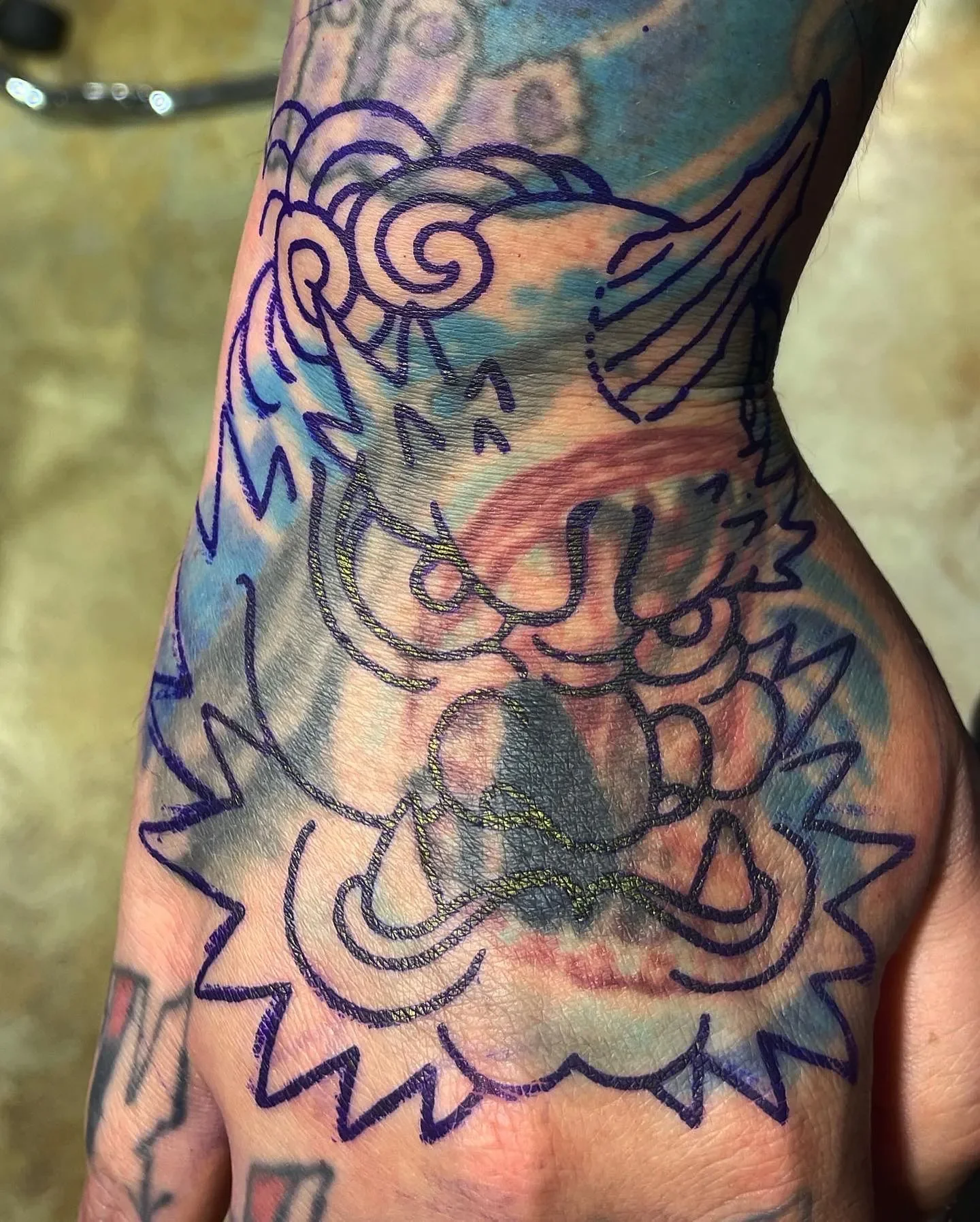 Close-up of a tattoo on a person's arm with outlined floral and decorative designs, some parts are filled with color.