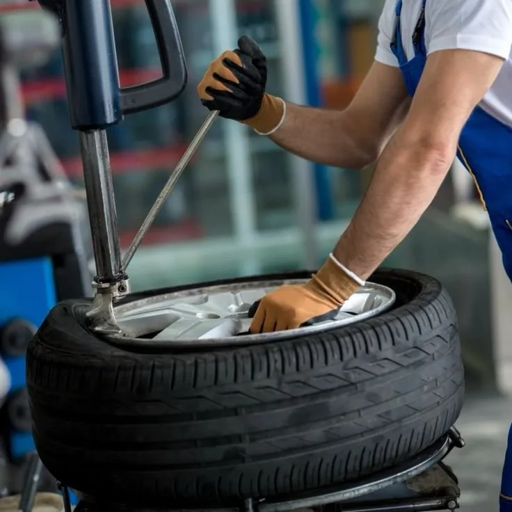 Automotive technician operating a tire changer machine during tire mounting and balancing service.
