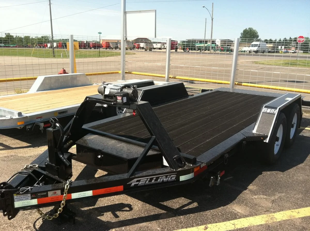 Black flatbed vehicle trailer parked in front of repair shop lot.