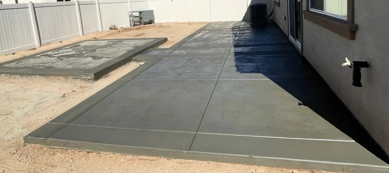 Newly poured concrete patio and a smaller concrete slab in a backyard, separated by a border, with a fence in the background.