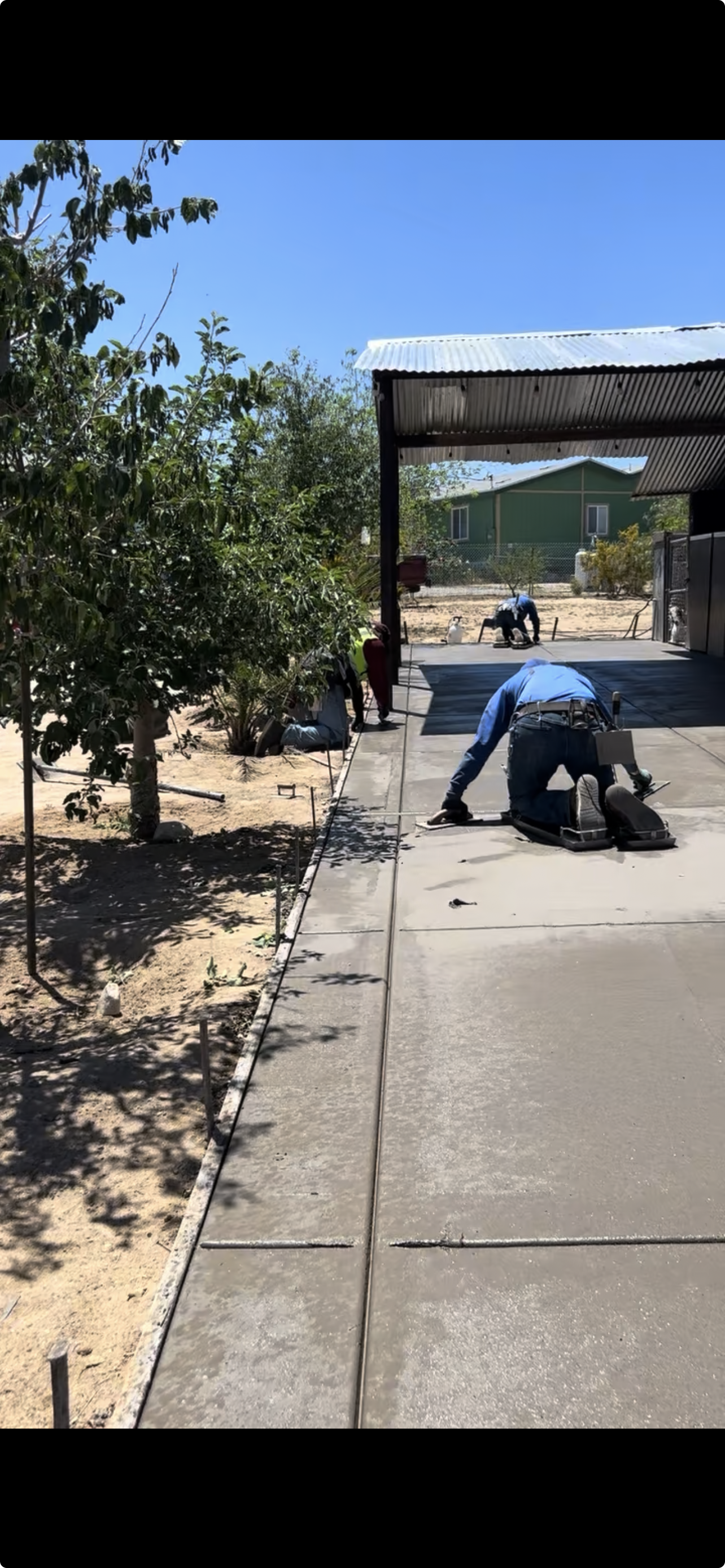 Workers installing a concrete sidewalk outside a horse stable on a sunny day.