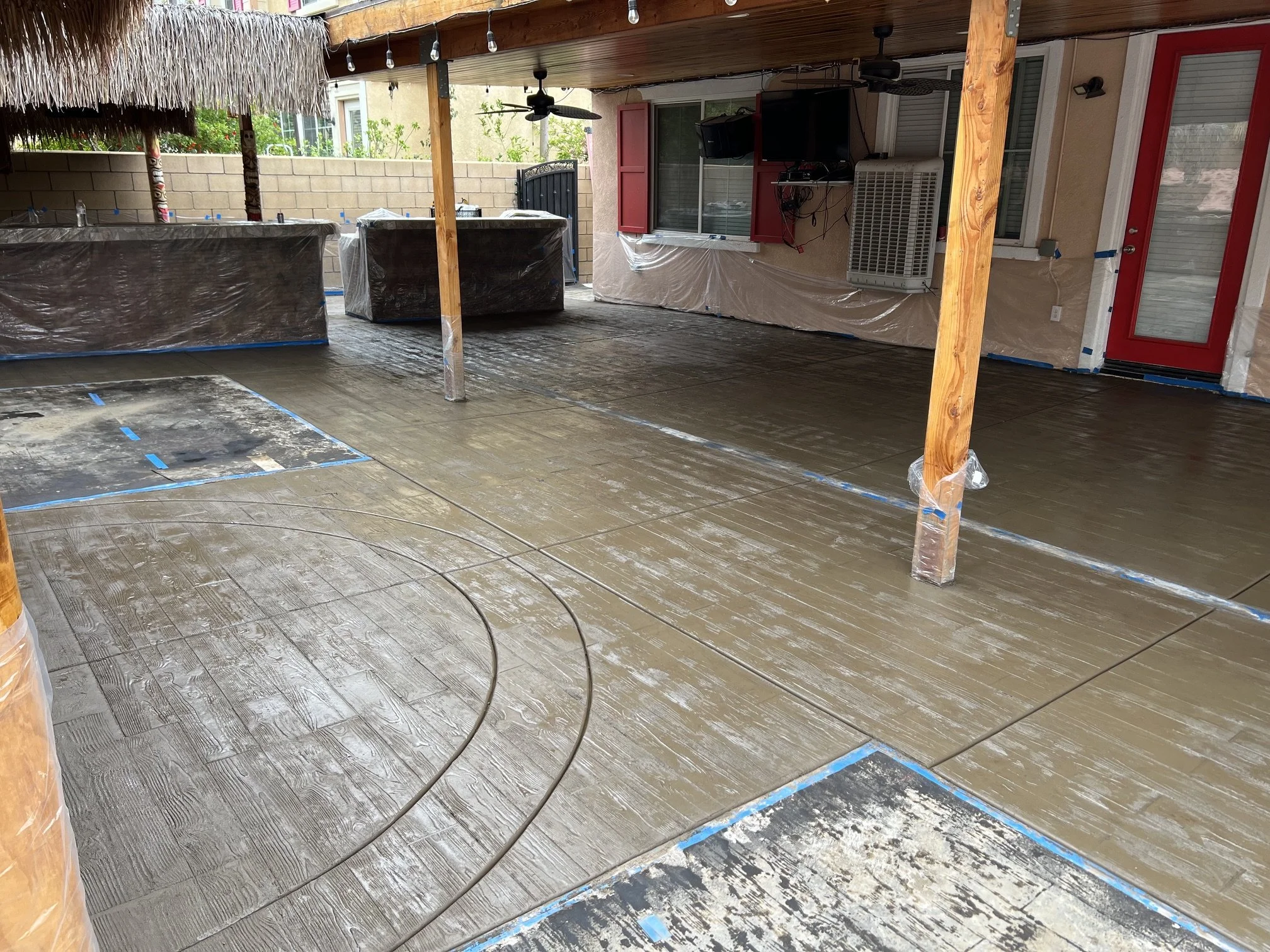 Covered patio with a ceiling fan, television, air conditioning unit, and glass sliding door. The floor is newly installed wood-like flooring with some areas still covered or taped for protection or installation.
