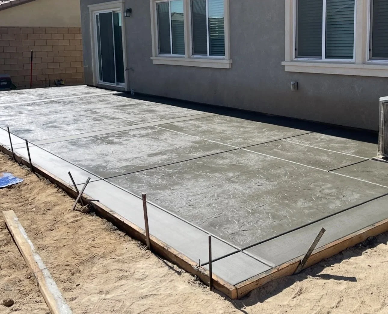 Concrete patio under construction next to a house, with wooden formwork and rebar in place.
