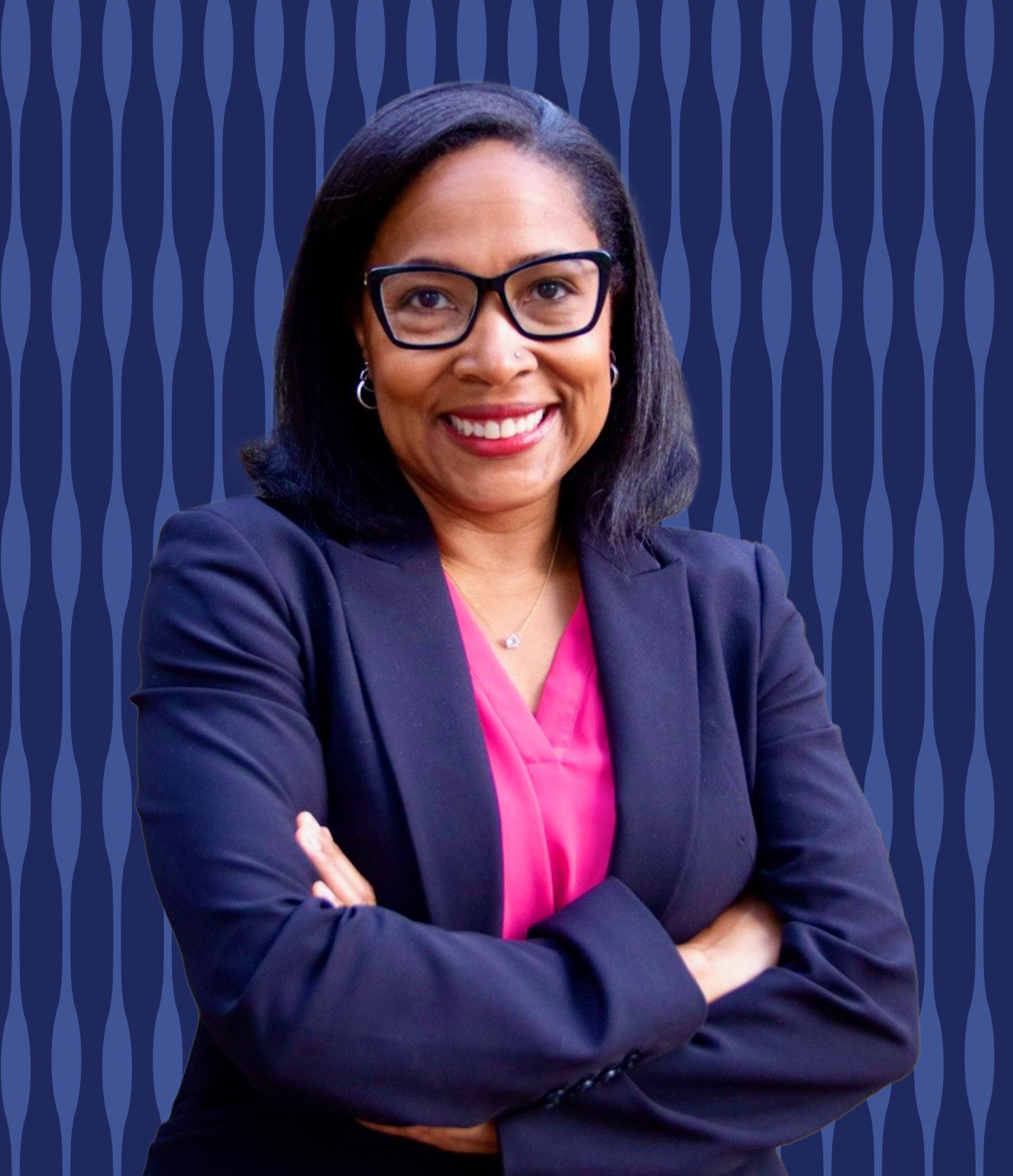 A woman with glasses, dark shoulder-length hair, and a sun nose piercing smiling with her arms crossed, wearing a navy blazer over a pink top, standing in front of a blue wavy patterned background.