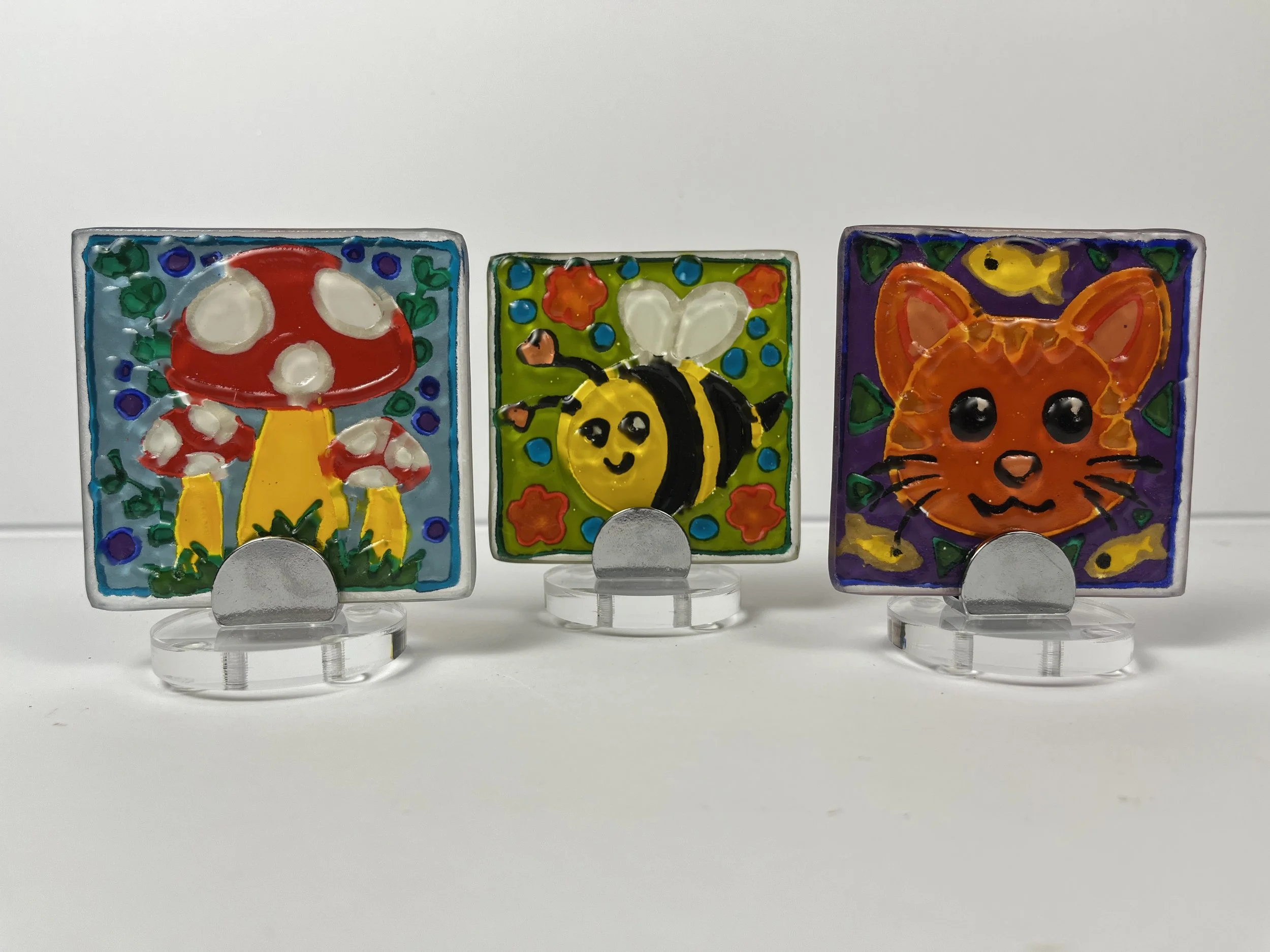 Mini textured glass tiles hand painted with simple fun designs  such as a bee, mushroom, and kitty