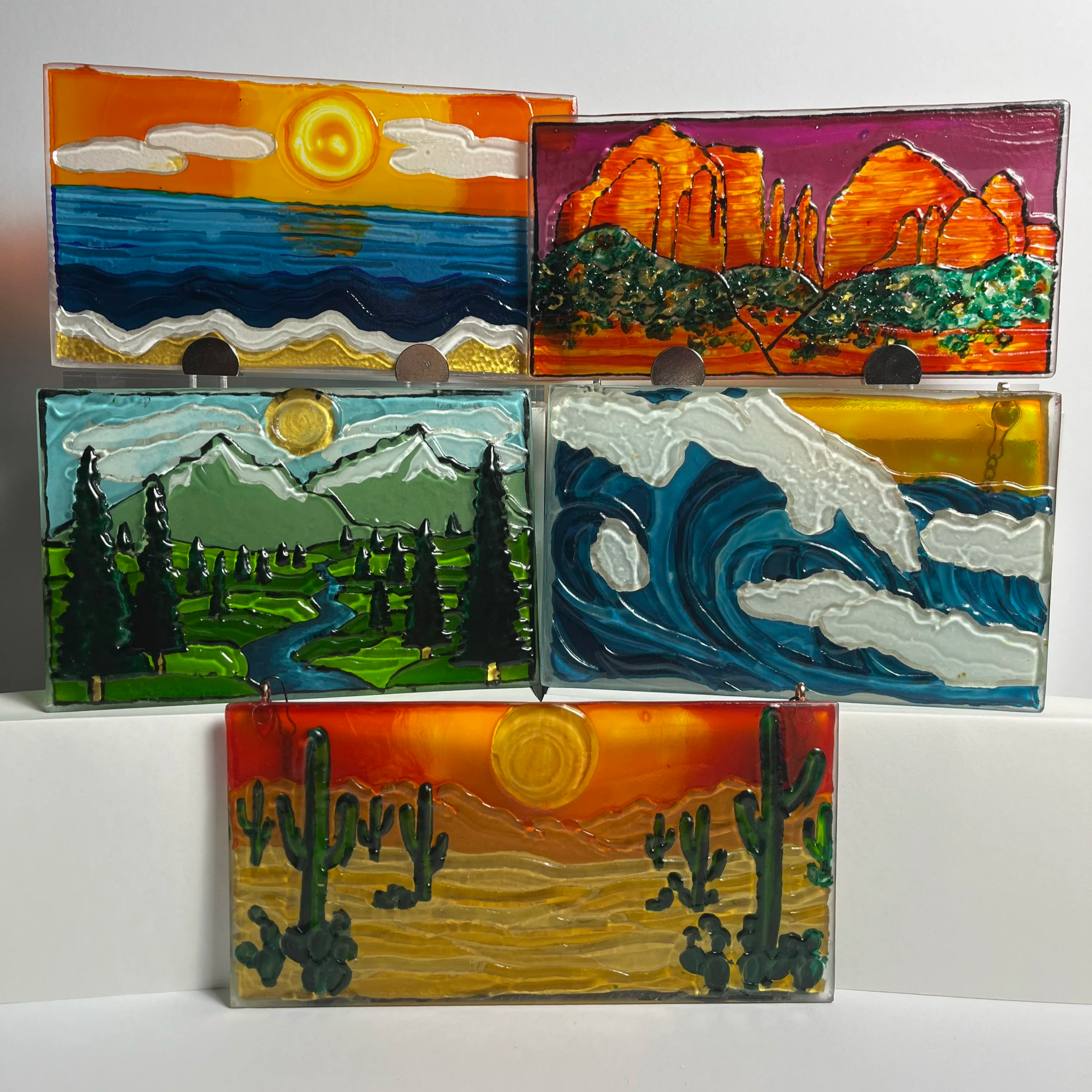 Various textured glass wall art and suncatchers hand painted with desert, ocean, beach, and mountain scenes