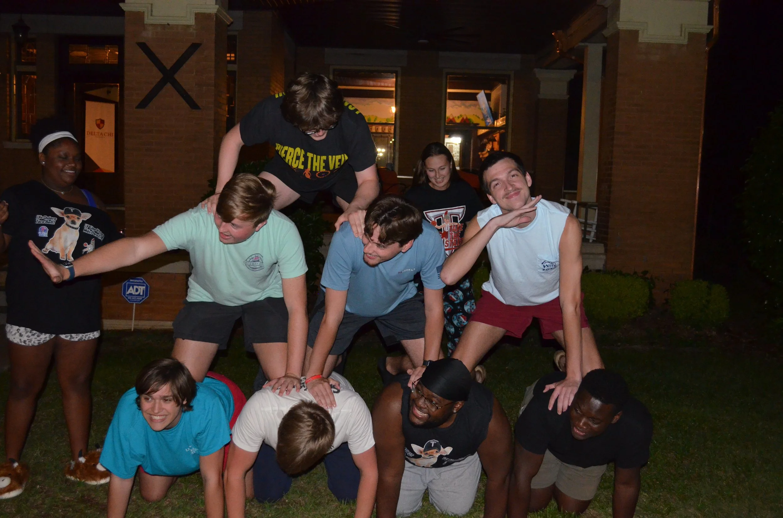 A group of young people forming a human pyramid outdoors at night, smiling and enjoying themselves.