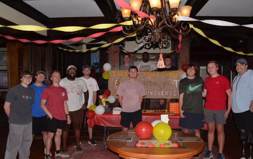 Group of young adults celebrating in a decorated room, with balloons, a cake, and a "Thank You Joey" poster in the background.