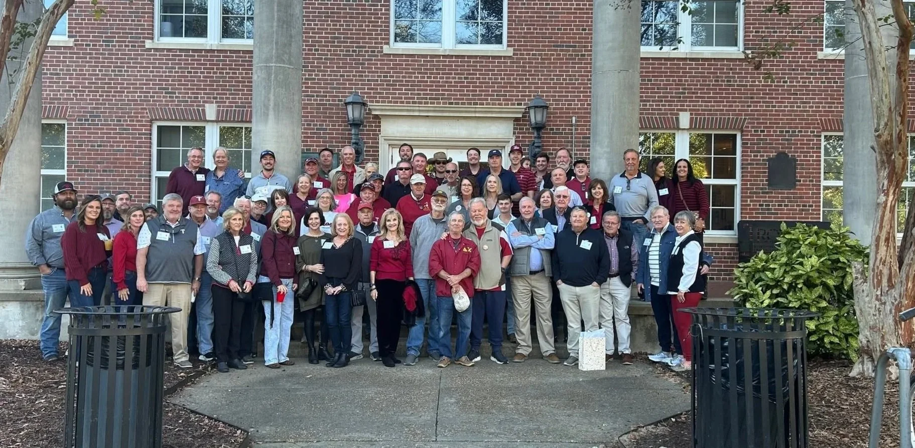 Group of people standing on steps outside brick building, posing for a group photo.