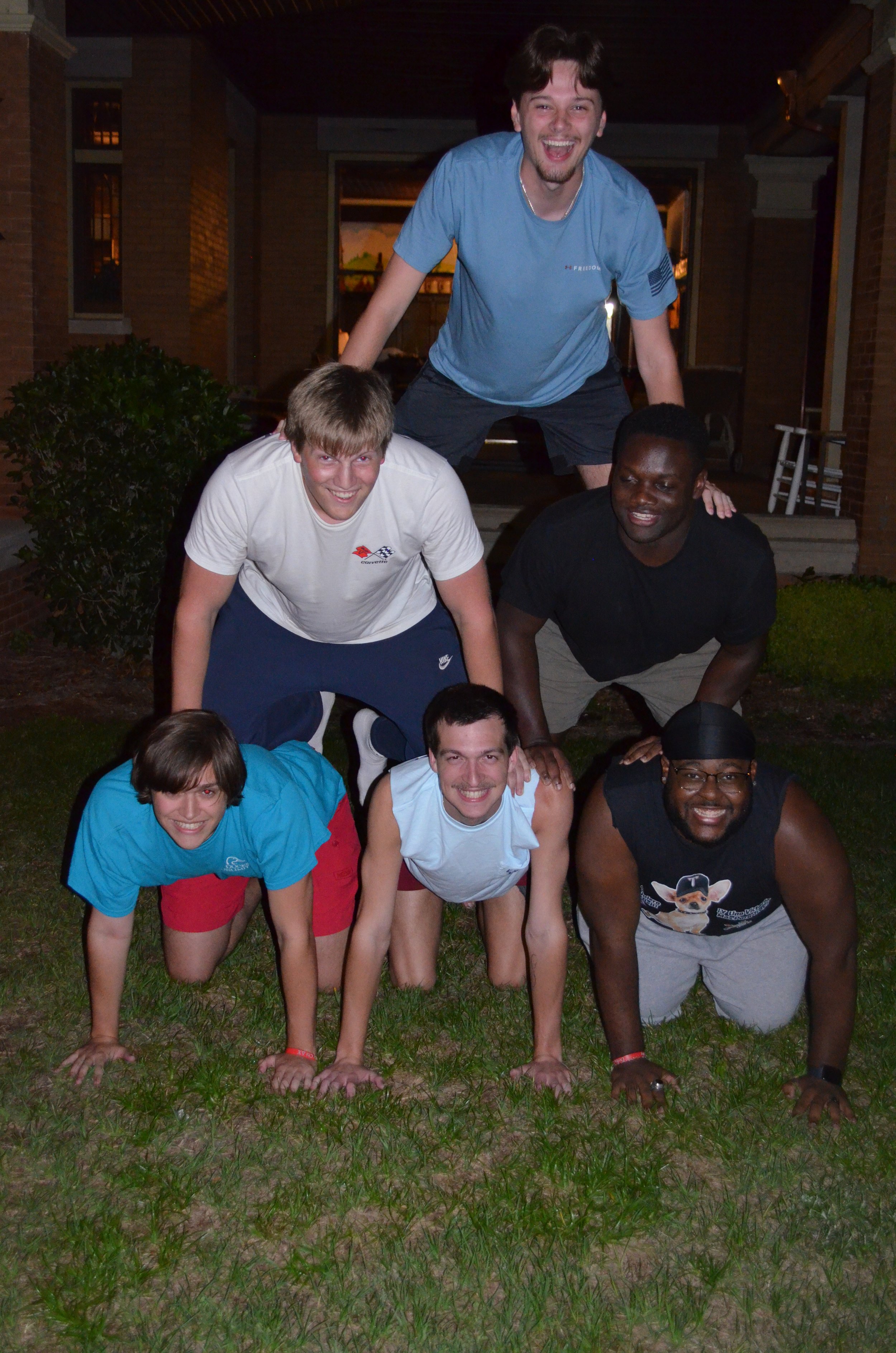 Group of people in a pyramid formation outside at night, smiling and posing for the photo.