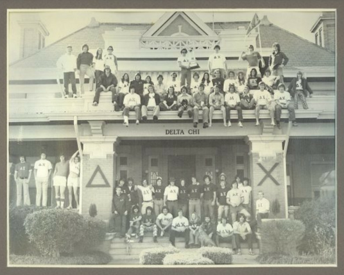 Group photo of fraternity members on the steps of a house with a sign that reads 'Delta Chi' in black letters.