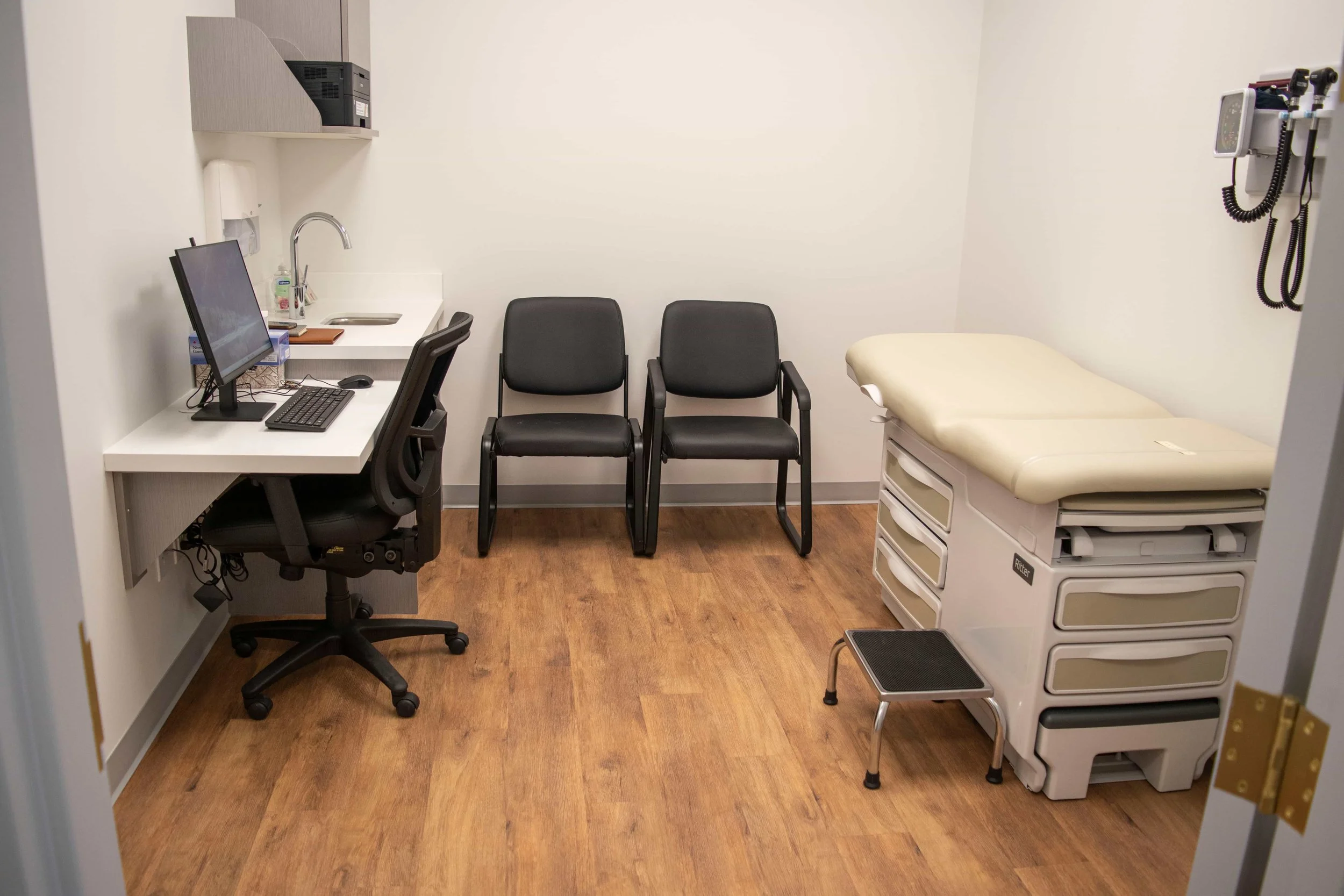 main doctor's office with two patient chairs and bed, a computer, printer and other clinical equipments