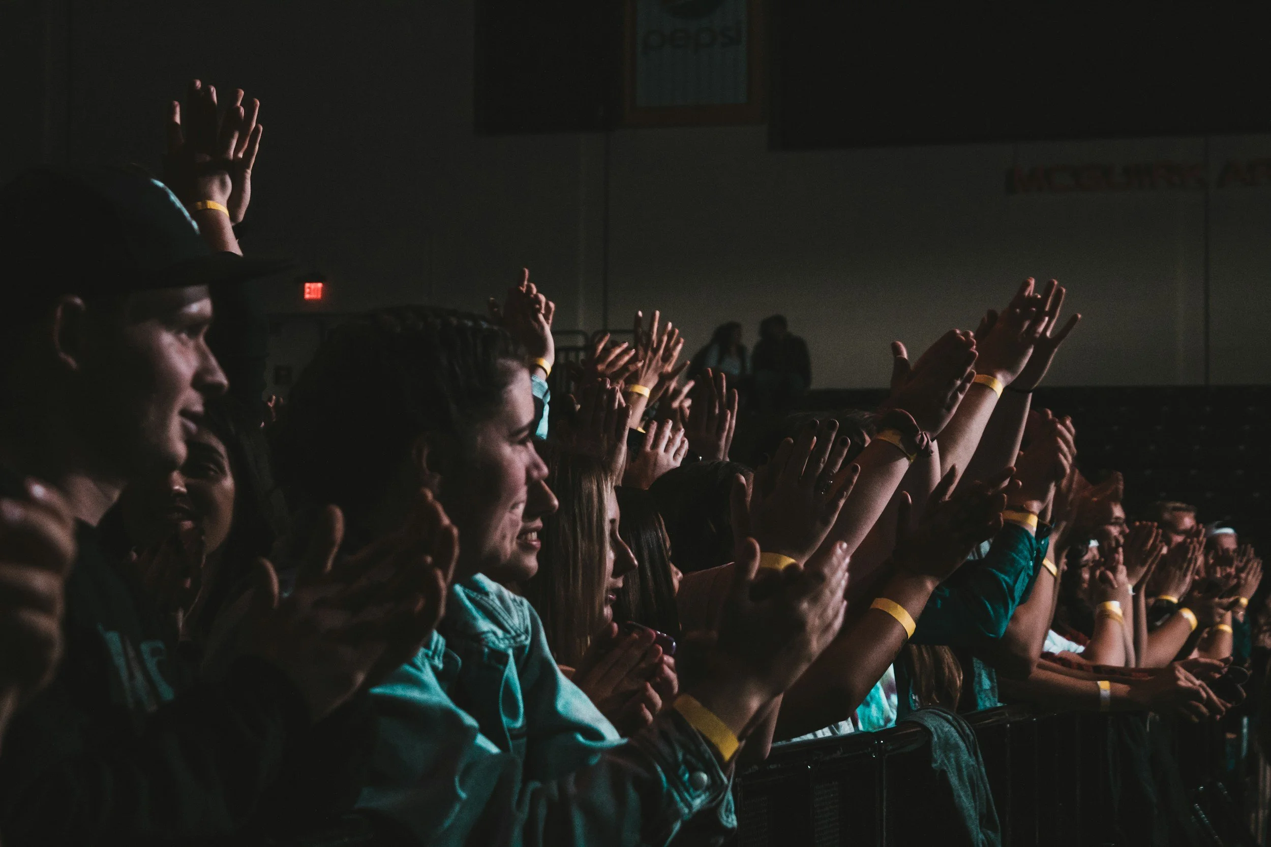 Audience members seated in a darkened venue, raising their hands during an event or performance.