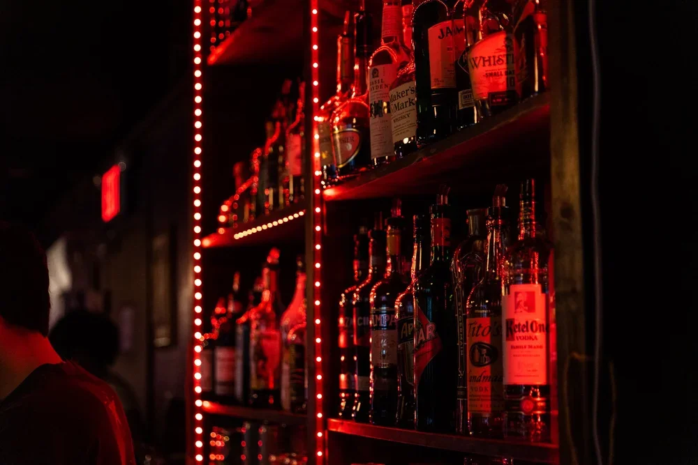 Bar shelf illuminated with red LED lights displaying various liquor bottles in a dark setting.