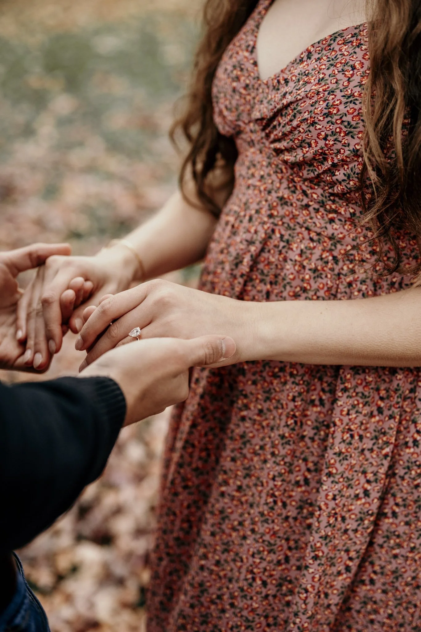 Two people exchanging a ring, focusing on their hands and the woman's ring finger, with autumn leaves in the background.