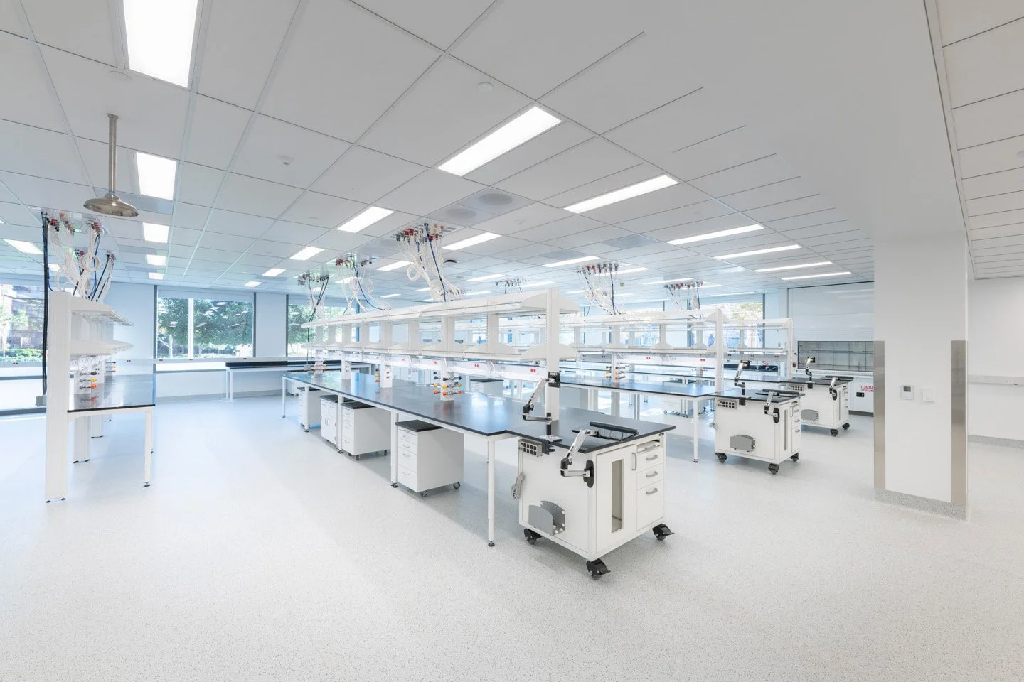 A modern laboratory with multiple workbenches and lab equipment, large windows, and bright overhead lighting.