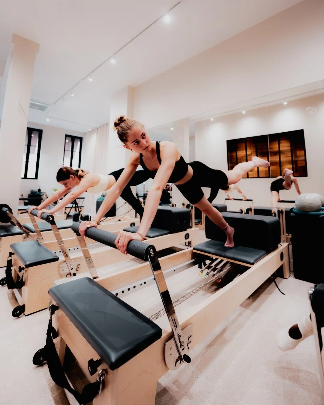 Groupe de femmes faisant de l'exercice sur des reformers Pilates dans un studio bien éclairé.