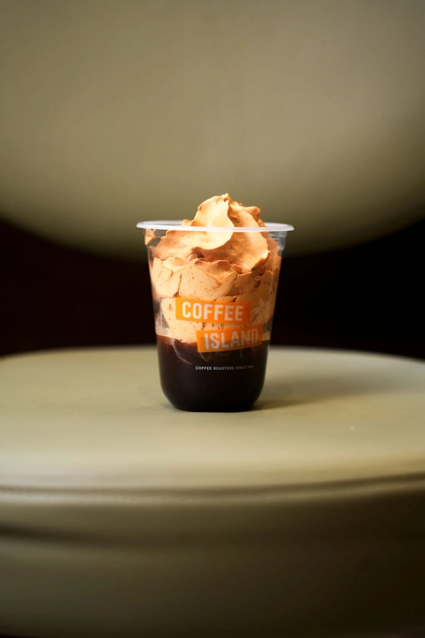 Un verre transparent avec une boisson glacée et de la crème fouettée, portant une étiquette orange avec le texte "COFFEE ISLAND".