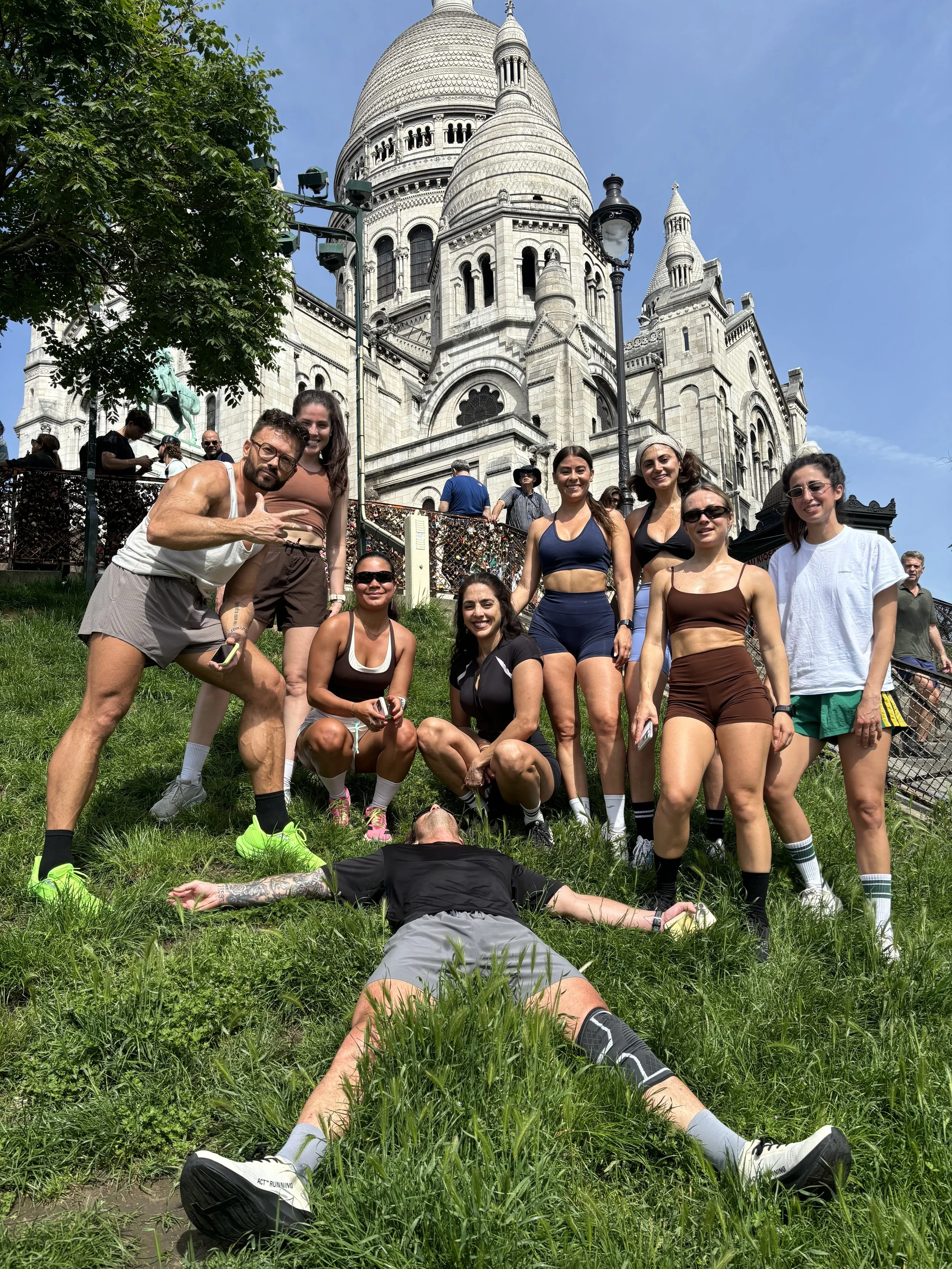 Groupe de personnes d'un club de run posant devant la basilique du Sacré-Cœur à Montmartre, Paris, avec un homme allongé en premier plan et une grande église en arrière-plan.