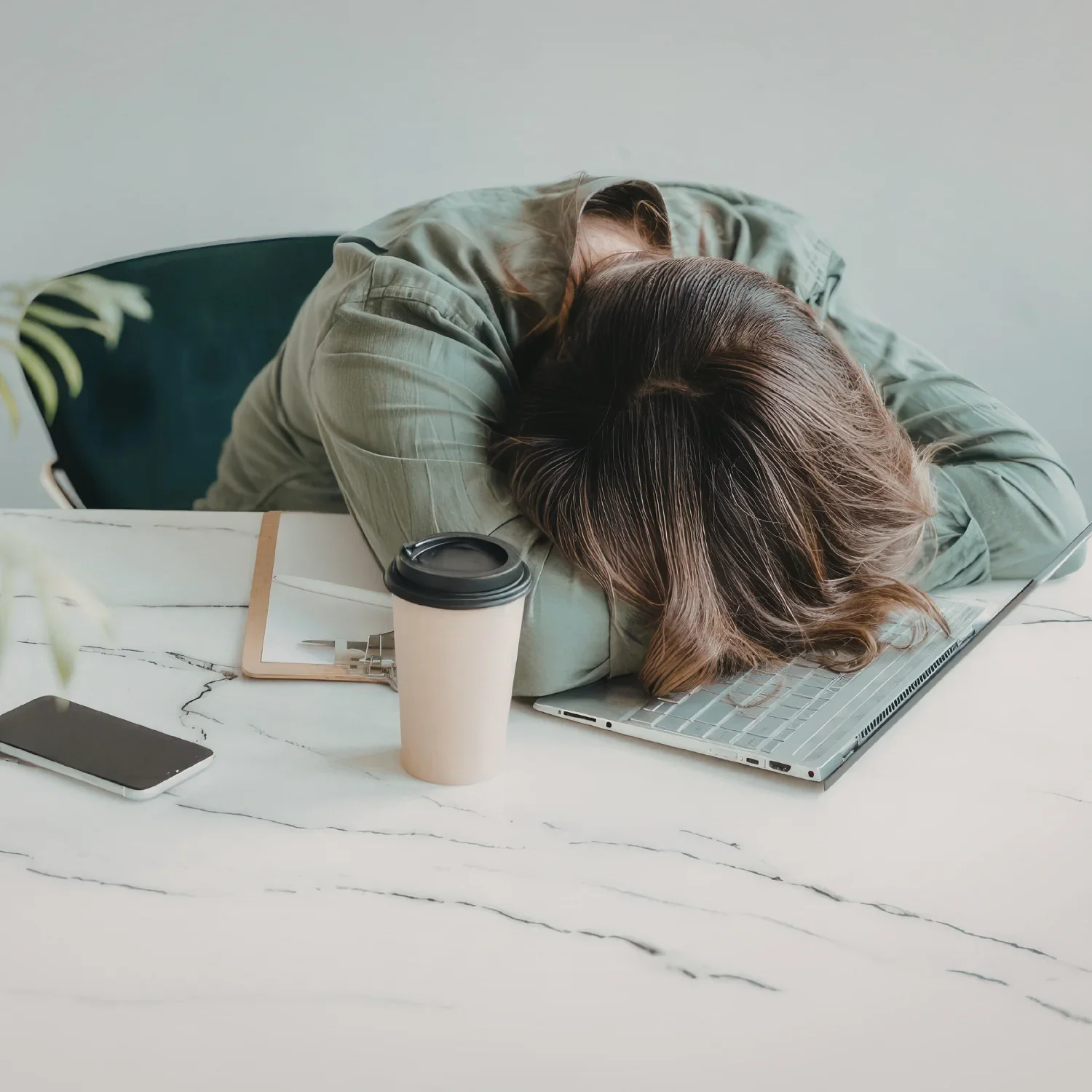 Two women are sleeping on a white table, with a laptop, a coffee cup, and a smartphone nearby.