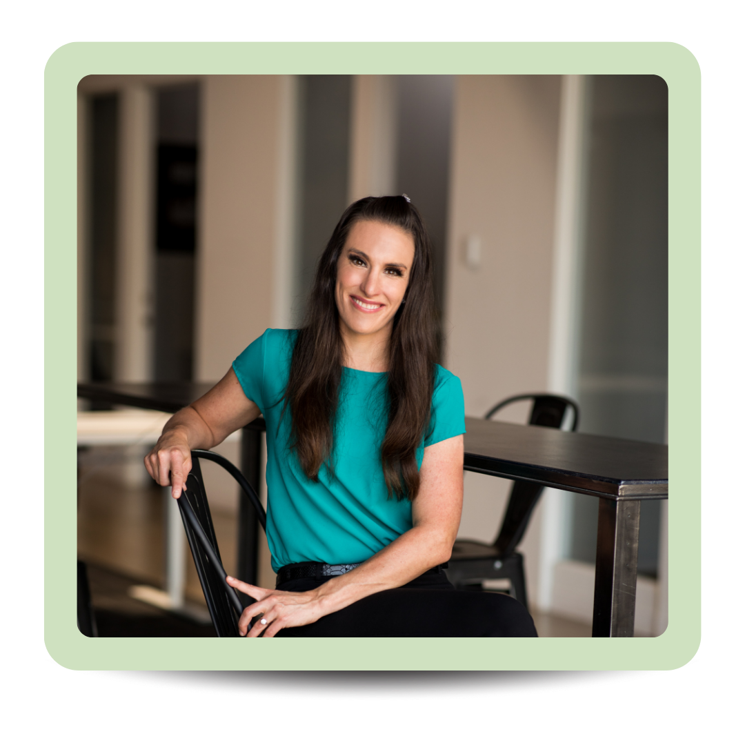 A woman with long dark hair, wearing a teal shirt, sitting at a table with a smile.